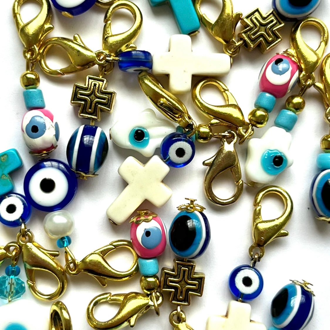 Assorted good luck charm beads including crosses, evil eye designs, and gold clasps on a white background