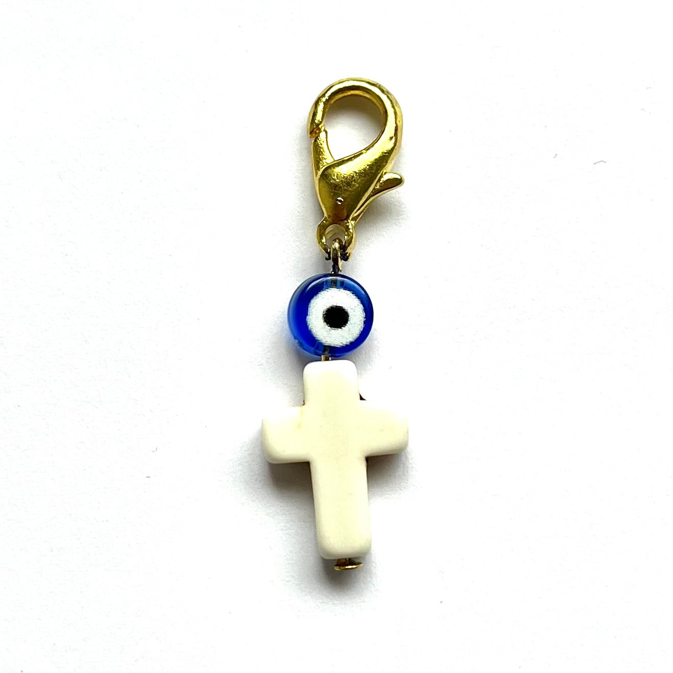 Howlite Cross charm with blue evil eye and gold clasp on white background