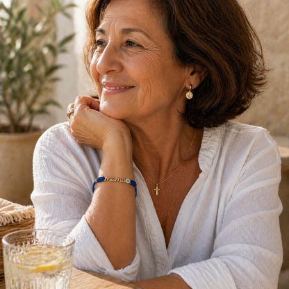 Woman in a white shirt sitting outdoors with a glass of water, wearing a mama bracelet with Evil Eye