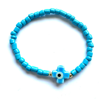 Mykonos mati stackable bracelets with ceramic evil eye charms. Blue beaded bracelet with a cross evil eye charm on a white background