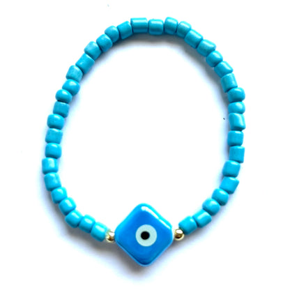 Mykonos mati stackable bracelets with ceramic evil eye charms. Blue square beaded bracelet with a square evil eye charm on a white background