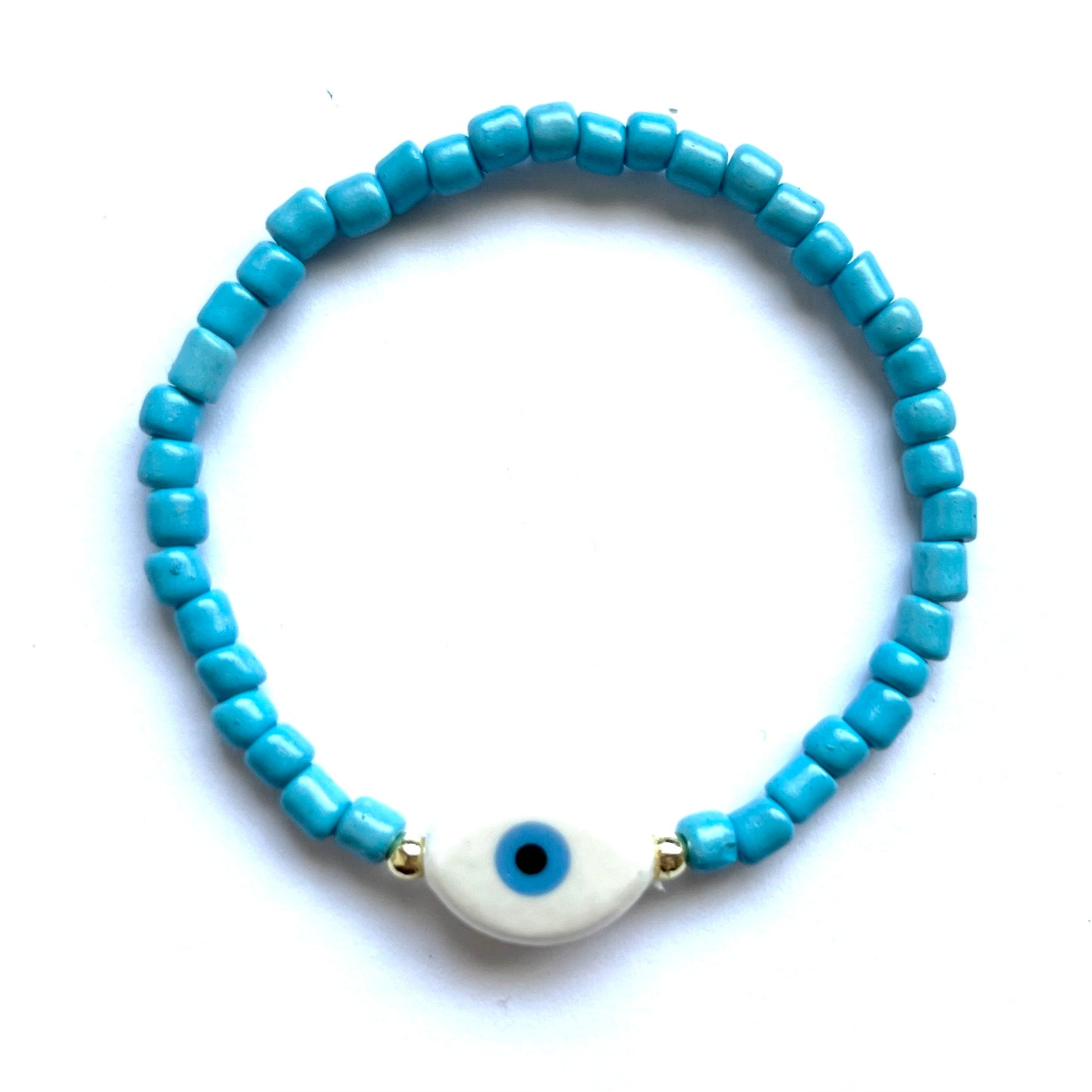 Mykonos mati stackable bracelets with ceramic evil eye charms. White beaded bracelet with a oval evil eye charm on a white background