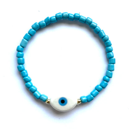 Mykonos mati stackable bracelets with ceramic evil eye charms. White beaded bracelet with a oval evil eye charm on a white background