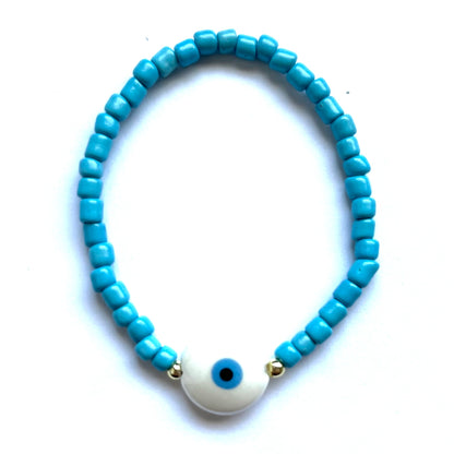 Mykonos mati stackable bracelets with ceramic evil eye charms. White beaded bracelet with a round evil eye charm on a white background