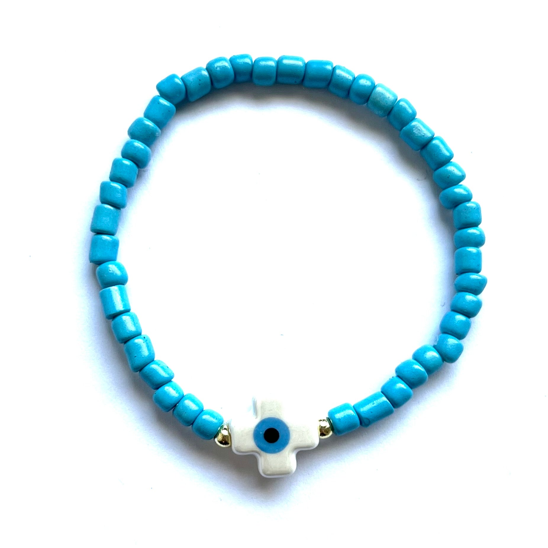 Mykonos mati stackable bracelets with ceramic evil eye charms. White beaded bracelet with a cross evil eye charm on a white background