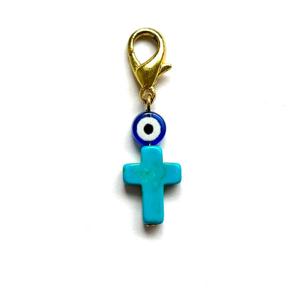 Turquoise cross charm with evil eye design on a white background